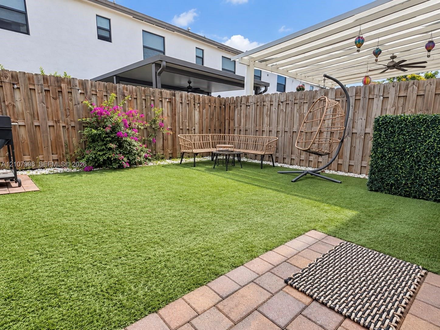 Private backyard featuring synthetic turf, paver patio, wood privacy fencing, and an overhead trellis