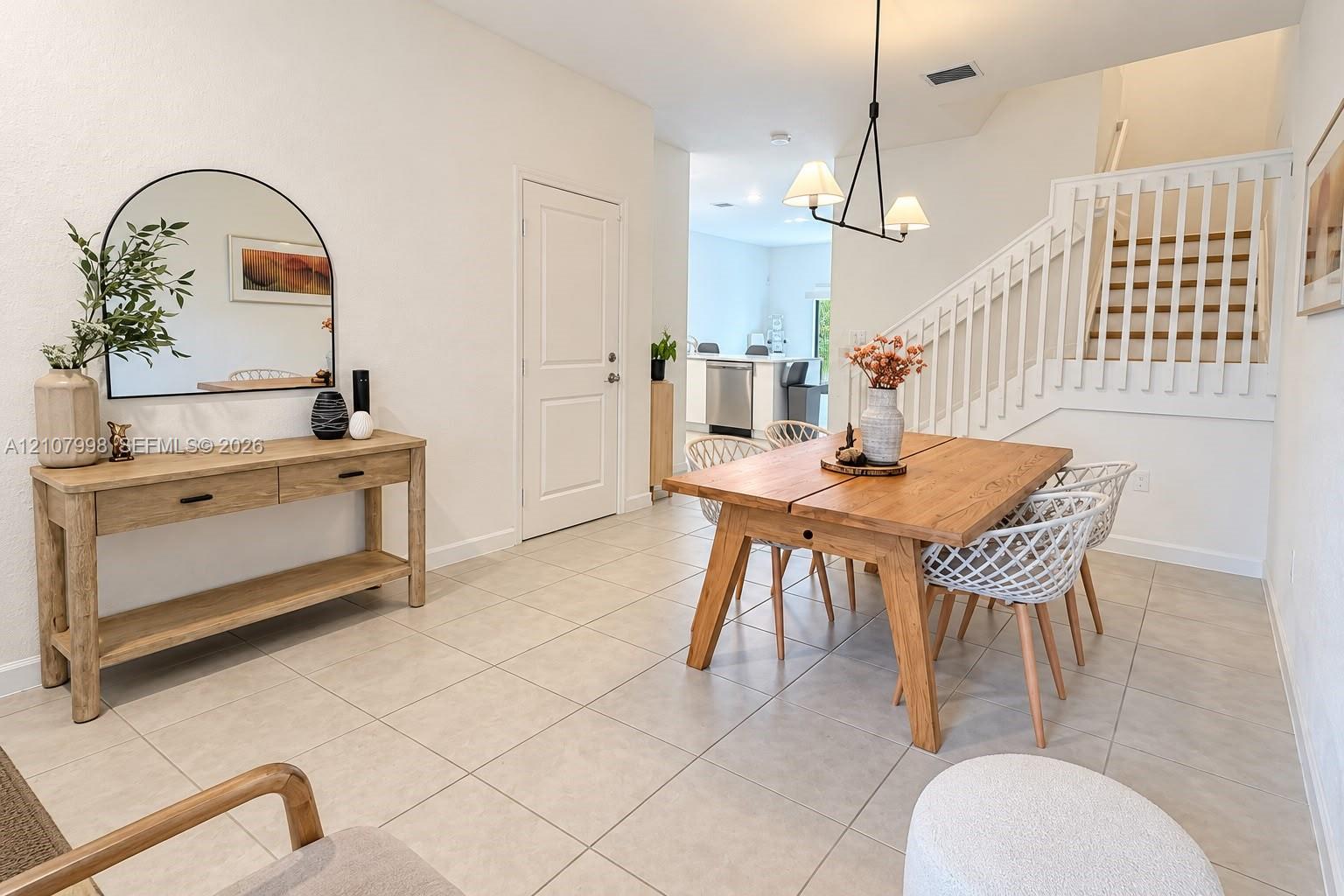Neutral tile flooring, staircase with white wooden balusters and wood-tread steps, contemporary dual-light pendant fixture, and white interior doors