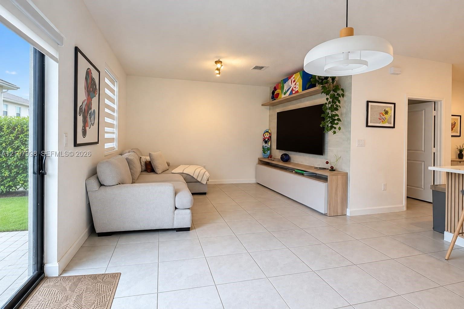 Living area featuring large format tile flooring, sliding glass patio doors, built-in media console with light wood finishes, and modern pendant lighting