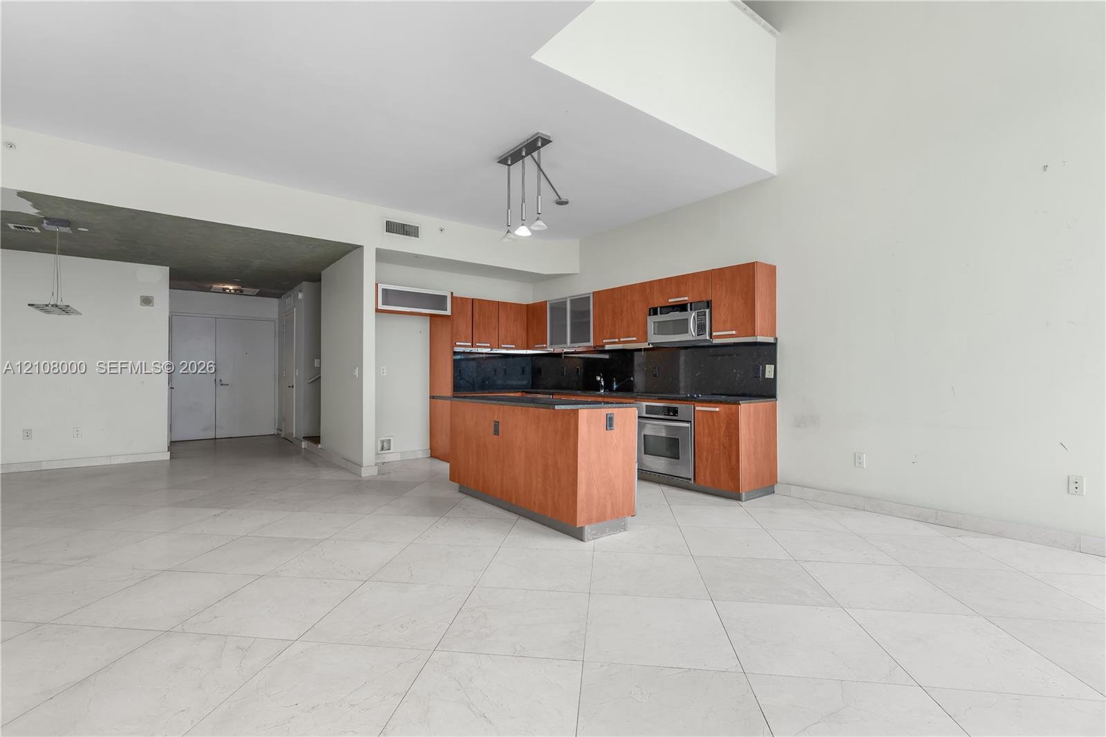Kitchen featuring wood-tone cabinetry, central island, integrated stainless steel appliances, and tile flooring