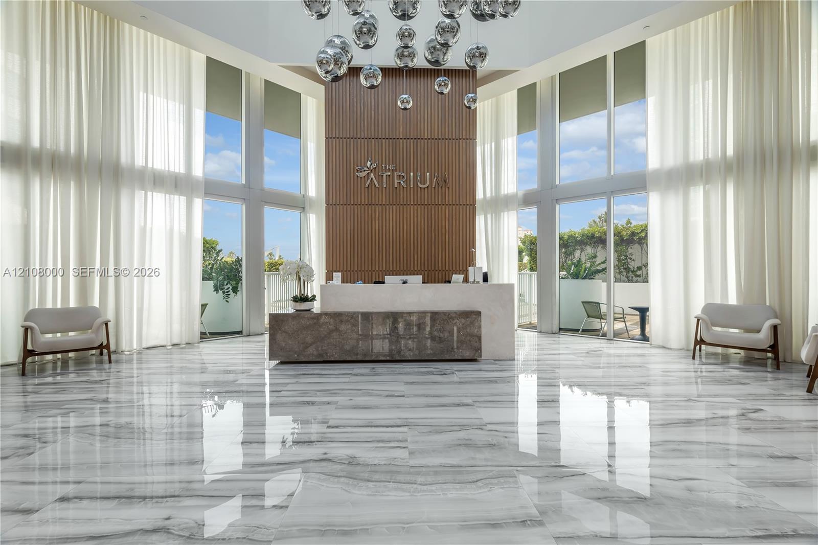 Double-height ceiling, floor-to-ceiling windows, polished stone flooring, custom vertical wood-slat feature wall, and tiered spherical pendant lighting