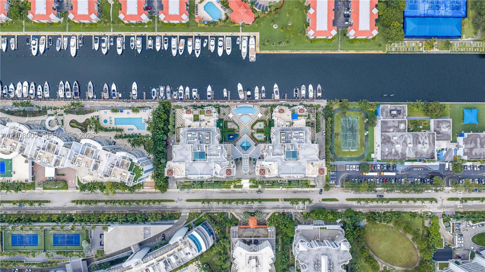 Aerial perspective of a waterfront residential complex featuring direct canal access, boat slips, paved parking, swimming pools, and sports courts