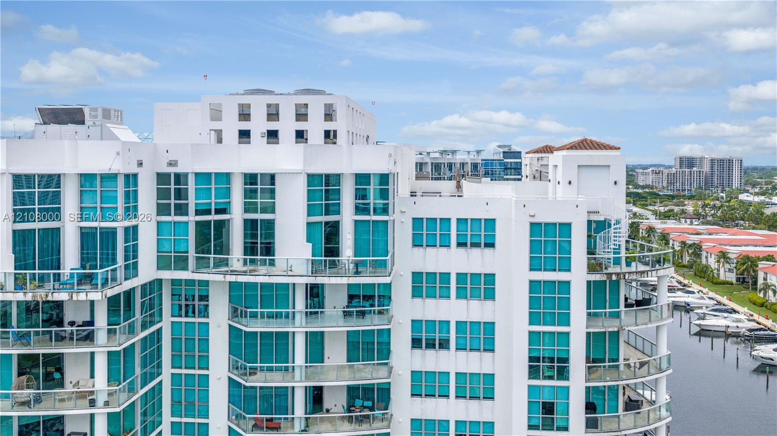High-rise exterior featuring a white stucco facade, floor-to-ceiling glass paneling, multiple levels of private glass-railed balconies, and a marina-front location