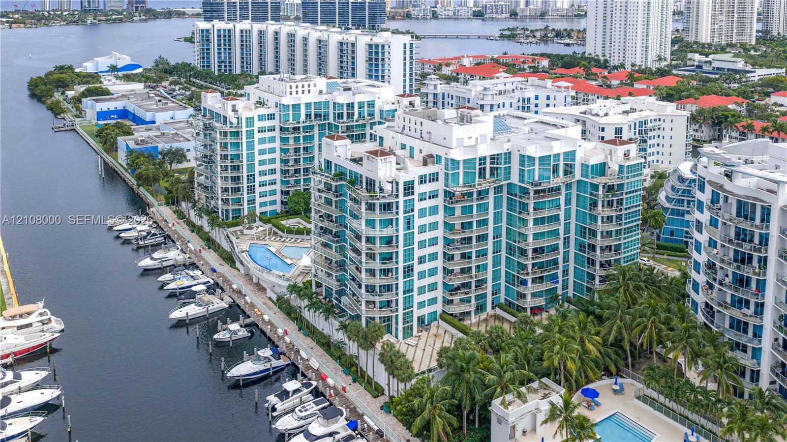 High-rise residential building featuring expansive glass paneling, wraparound balconies, deep-water boat slips, and a ground-level swimming pool