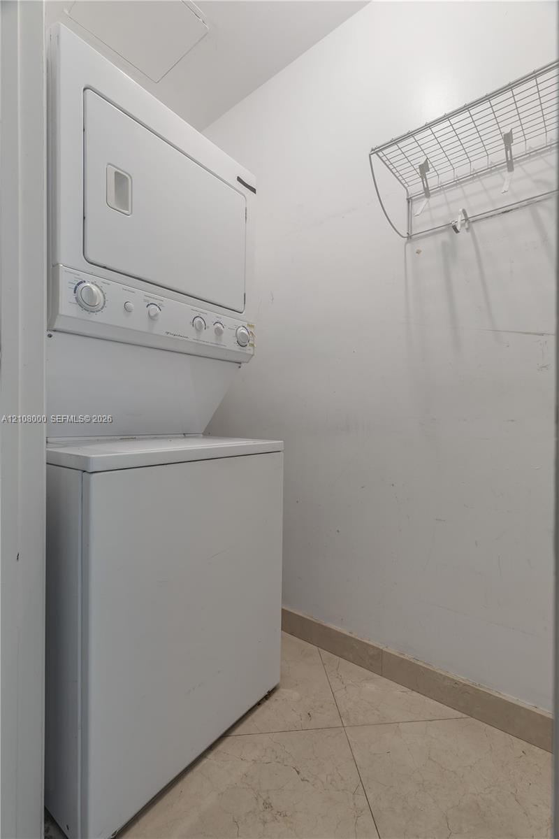 Stacked laundry unit with white finish, tile flooring, and integrated metal shelving