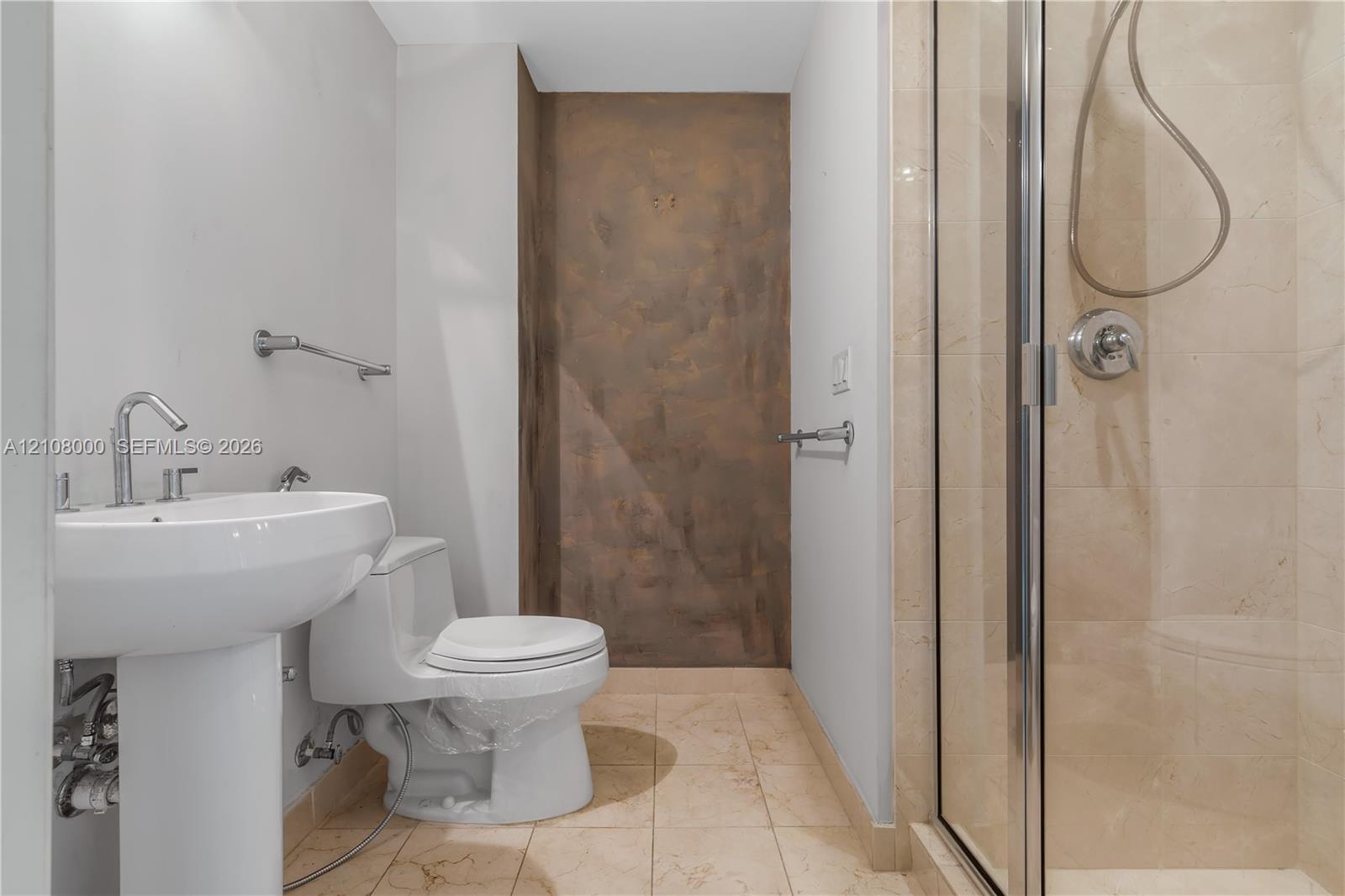 Bathroom featuring a pedestal sink, stone-finish floor tiling, glass-enclosed shower with stone-finish wall cladding, and metallic hardware