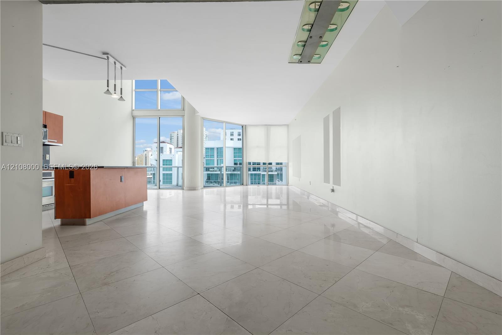 Open living area featuring large-format stone-finish flooring, floor-to-ceiling windows, a center kitchen island with dark surfacing, and contemporary recessed lighting