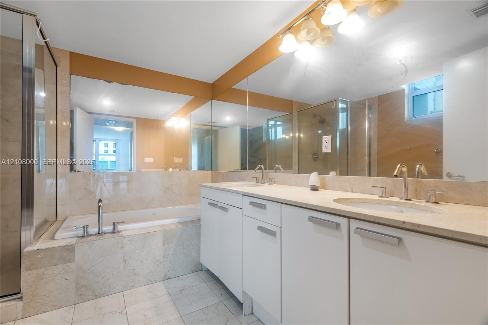 Bathroom featuring a stone-surround soaking tub, dual-sink vanity with light-toned countertop, full-width wall mirror, and a glass-enclosed shower
