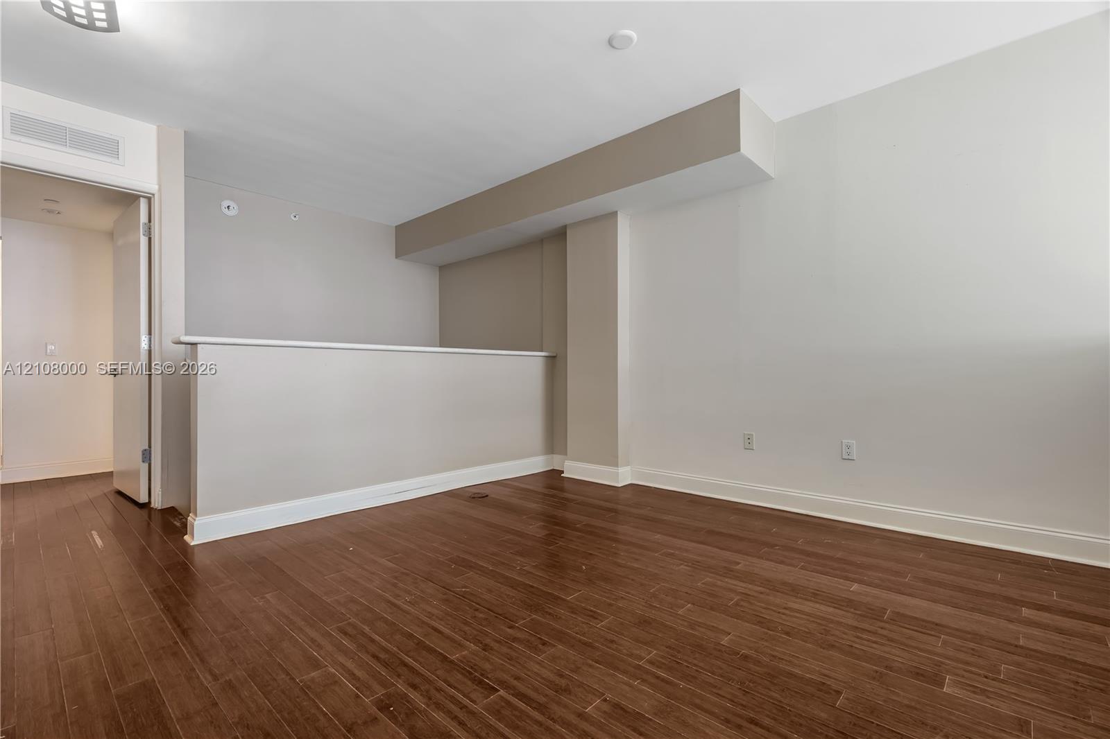 Interior space featuring wood-finish flooring, neutral wall tones, a partial height pony wall, and a structural soffit