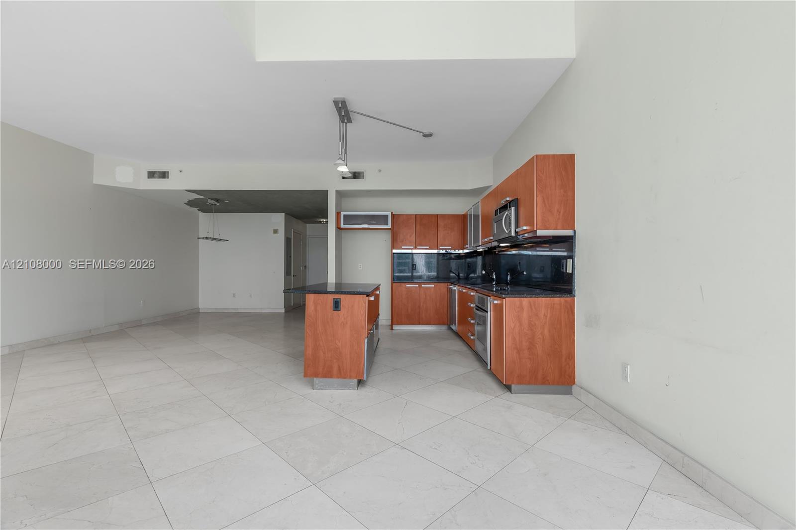 Kitchen featuring wood-veneer cabinetry, stone countertops, stainless steel appliances, a central island, and large-format tile flooring