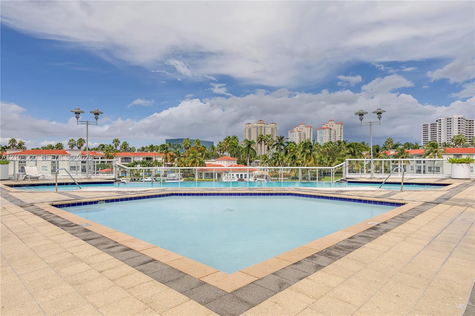Outdoor swimming pool featuring a light-toned tile deck, contrasting border tiles, and a white metal safety railing