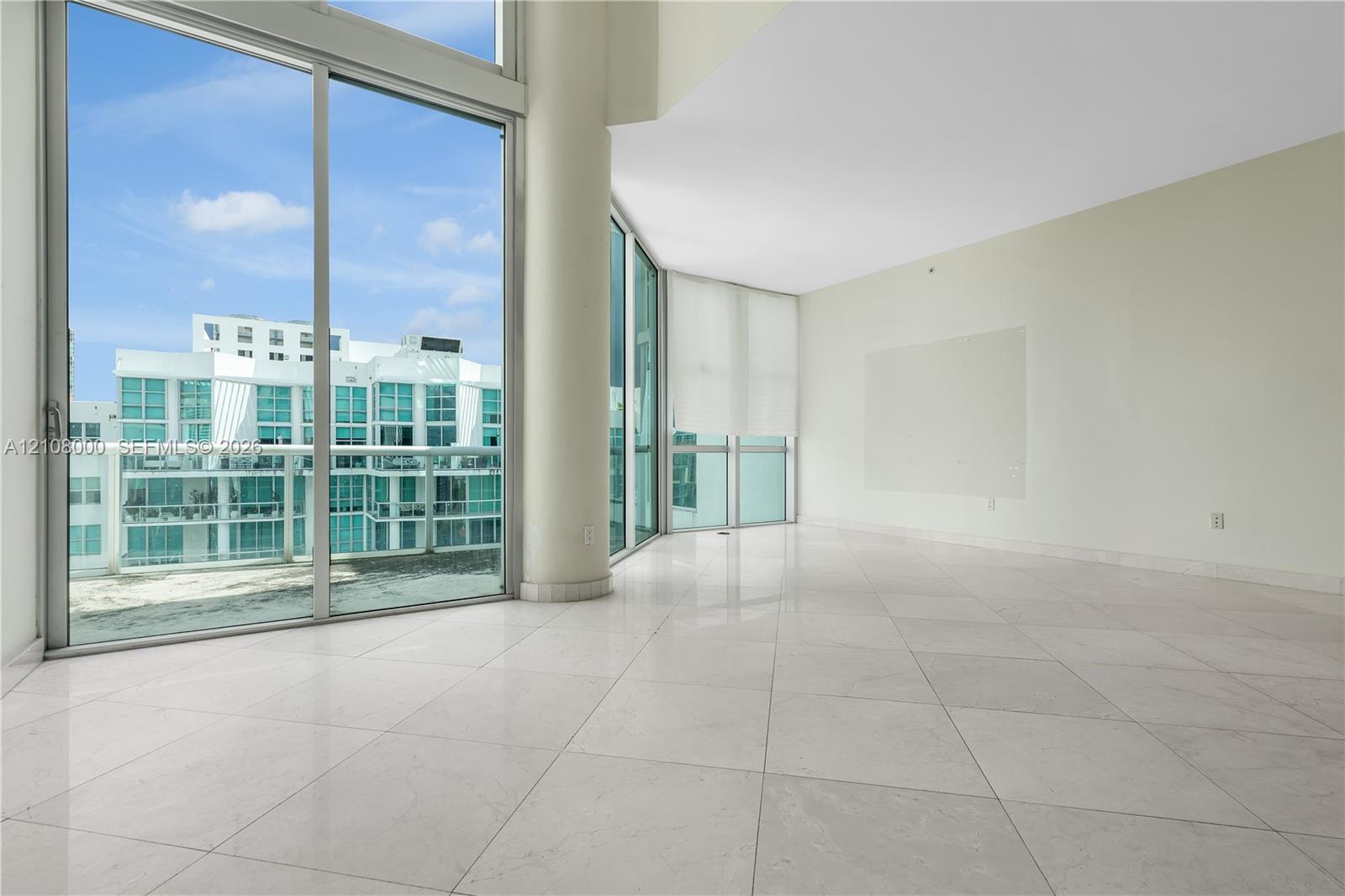Floor-to-ceiling glass windows, expansive stone flooring, structural support column, and glass-paneled exterior balcony