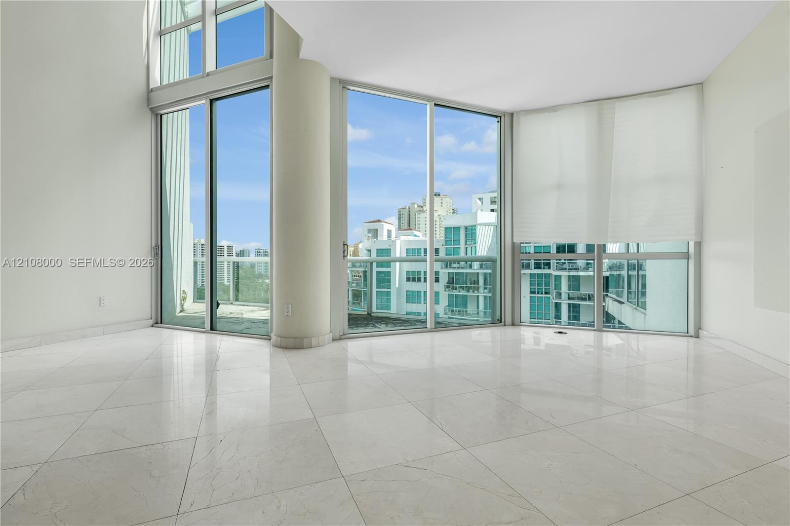 Floor-to-ceiling windows, high ceilings, large-format tile flooring, circular structural column, and glass-railing balcony