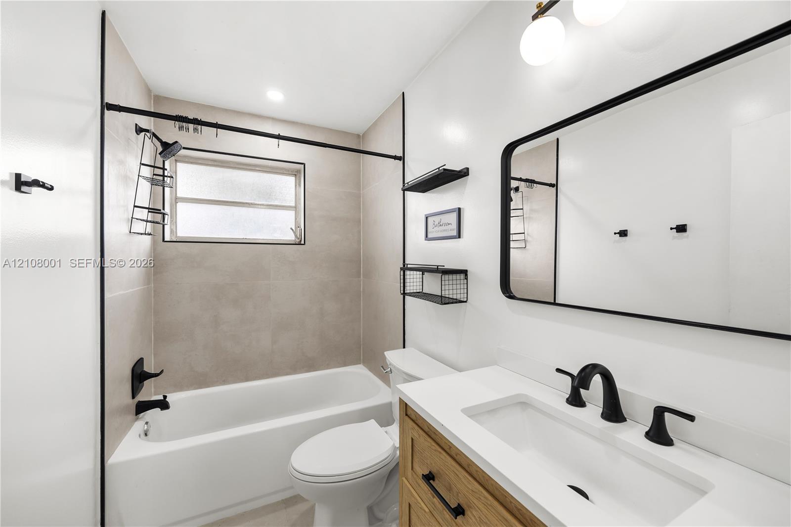 Bathroom featuring wood-finish cabinetry, a white countertop with an integrated basin, a matte black faucet, a tub-shower combination with floor-to-ceiling tile, and a rectangular mirror with a black frame