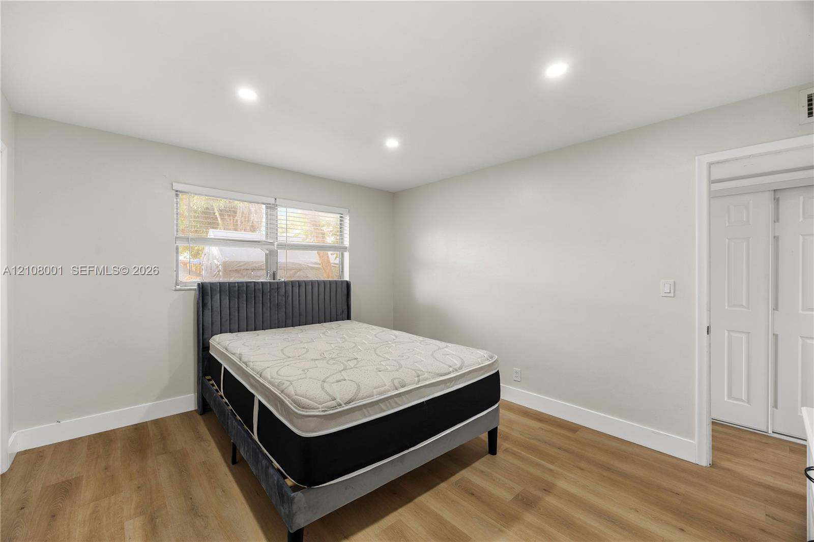 Room featuring wood-finish flooring, recessed lighting, double-pane window with blinds, and a built-in double-door closet