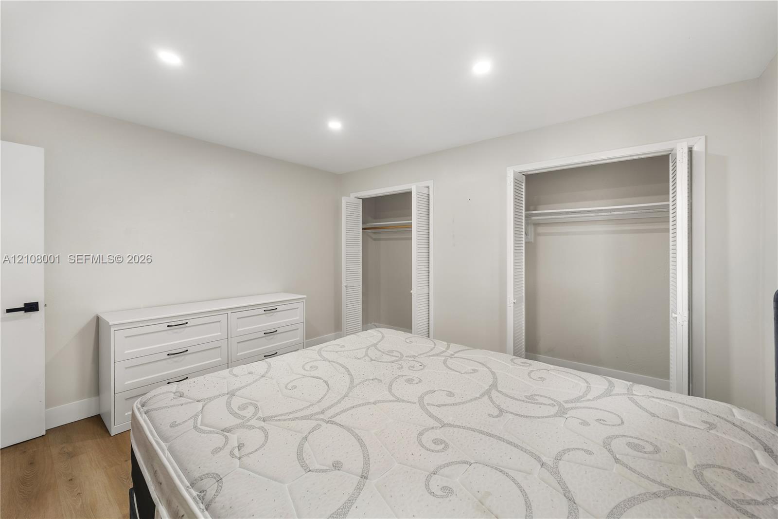 Neutral-toned interior featuring recessed ceiling lighting, wood-finish flooring, and dual closets with bifold louvered doors