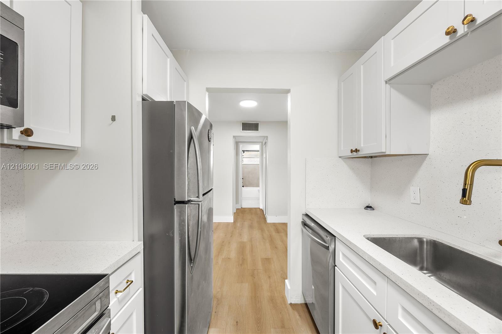 Kitchen featuring white Shaker-style cabinetry, light-toned composite countertops, stainless steel appliances, and wood-finish flooring