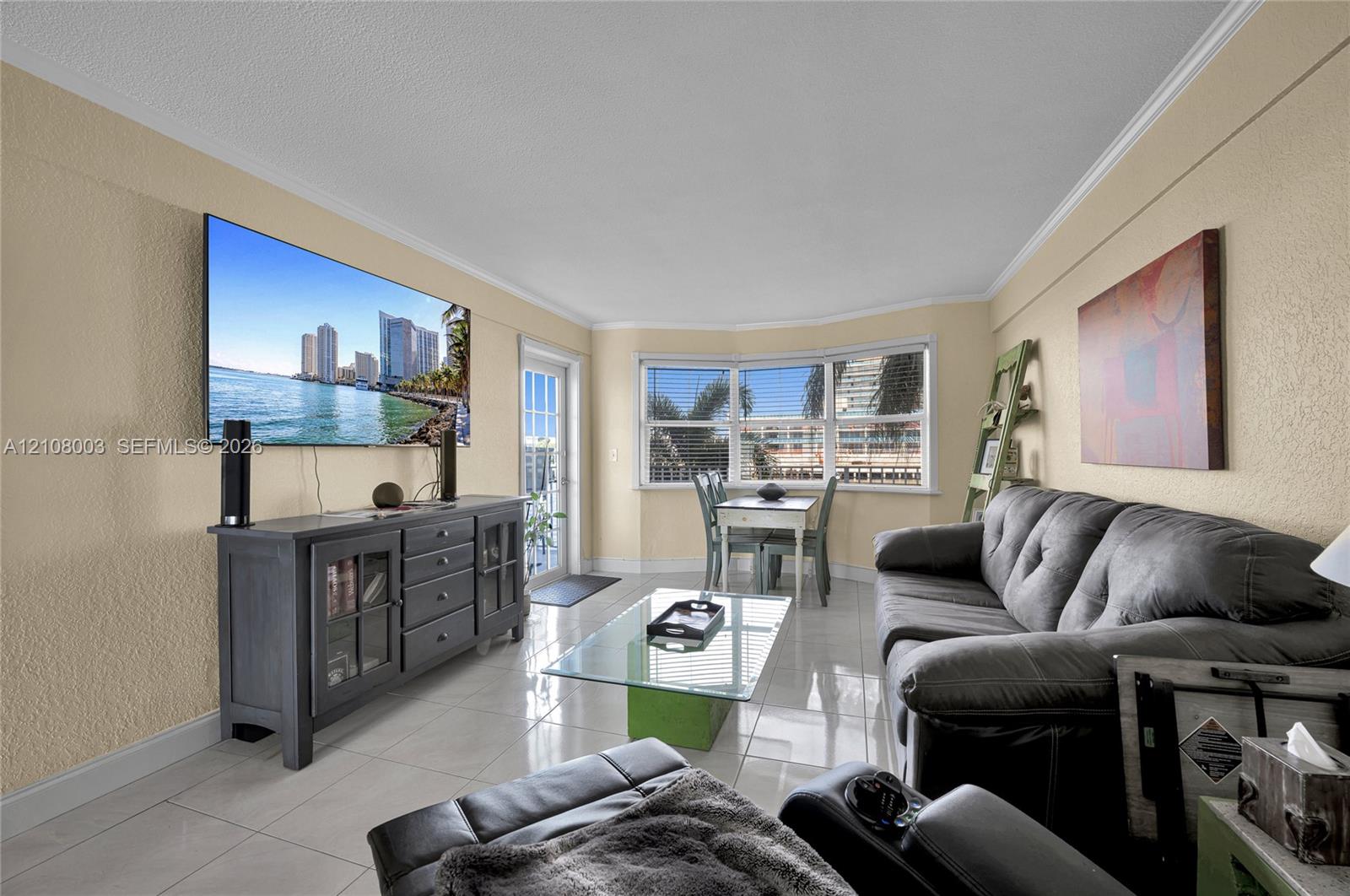 Living space featuring large-format tile flooring, crown molding, a multi-pane bay window, and a glass-paned door