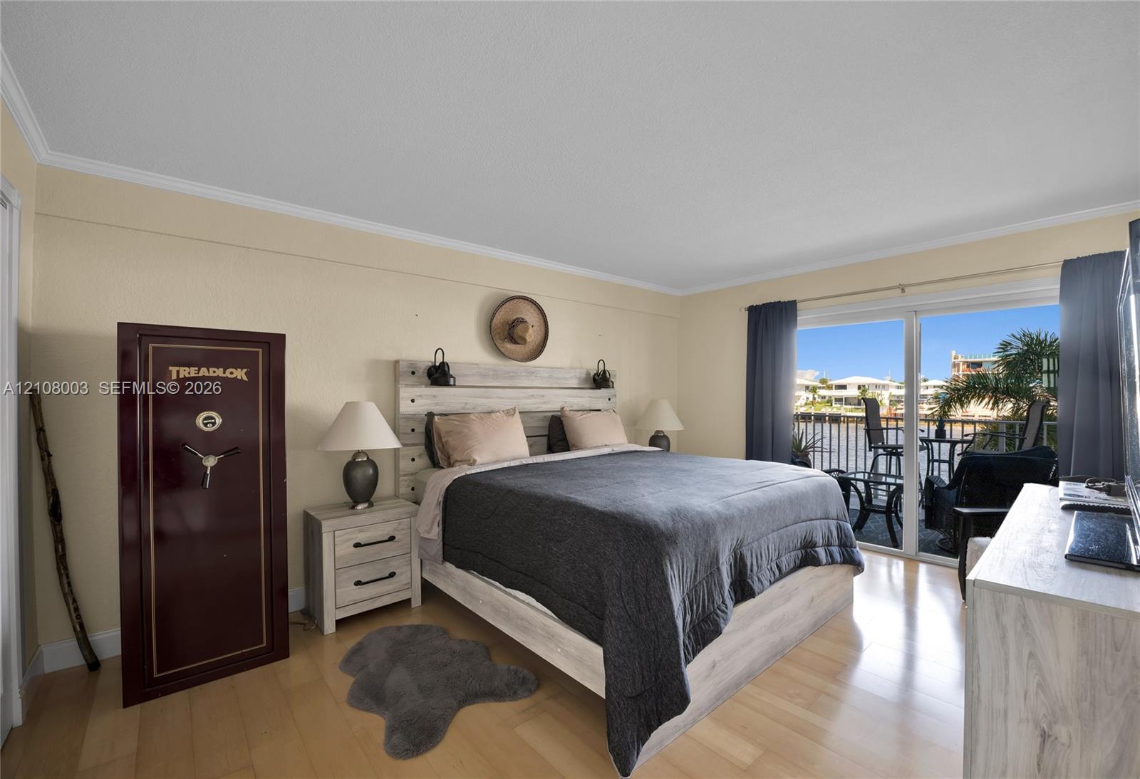 Sliding glass doors opening to a waterfront balcony, light-toned wood-finish flooring, and crown molding