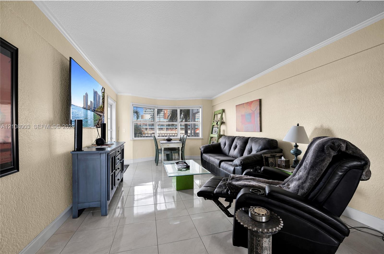 Living area featuring light-colored tile flooring, textured wall finishes, and a bay window