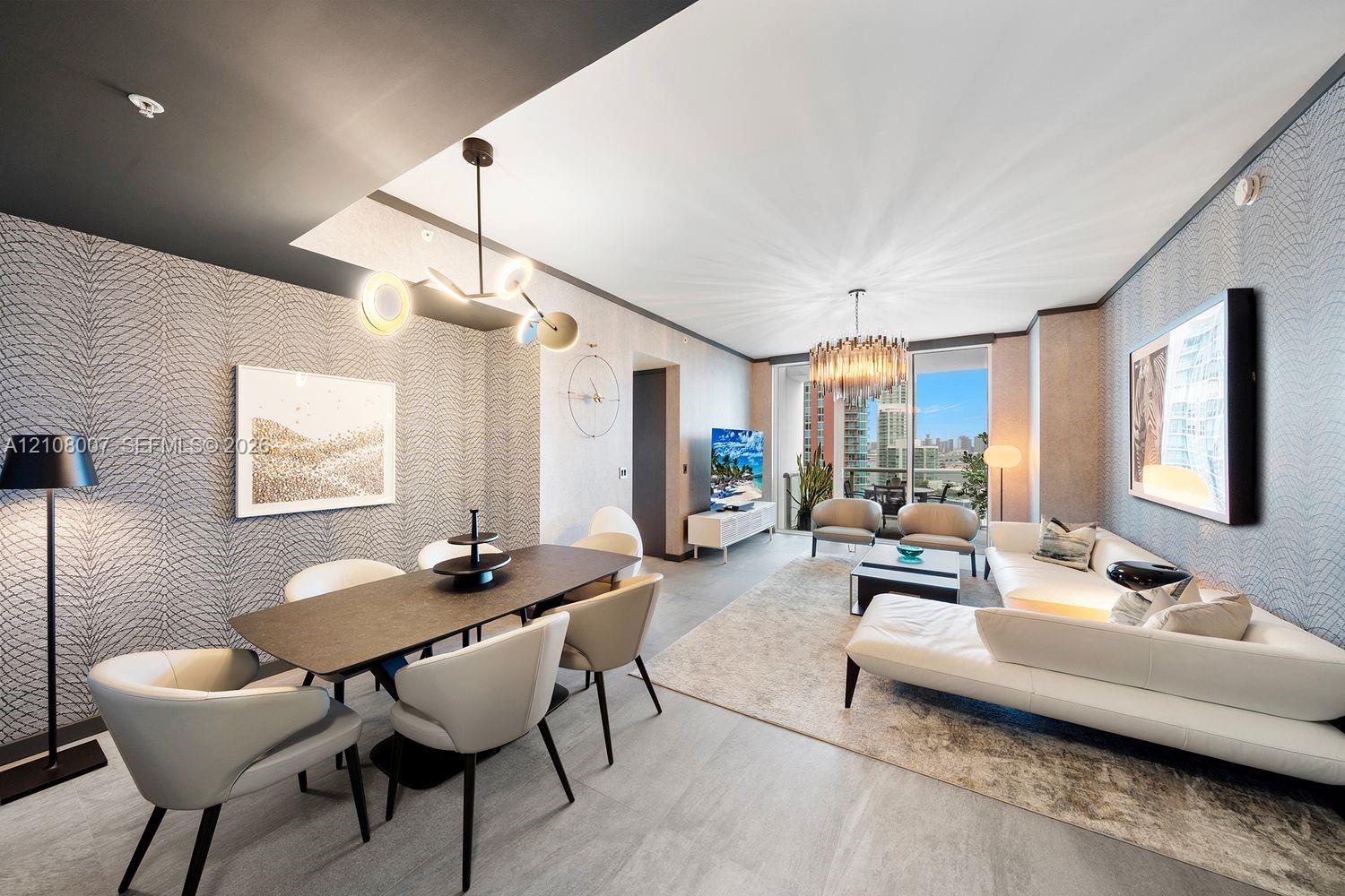 Open-concept living area featuring textured wall coverings, multi-arm contemporary pendant lighting, recessed ceiling architecture, and large-format tile flooring