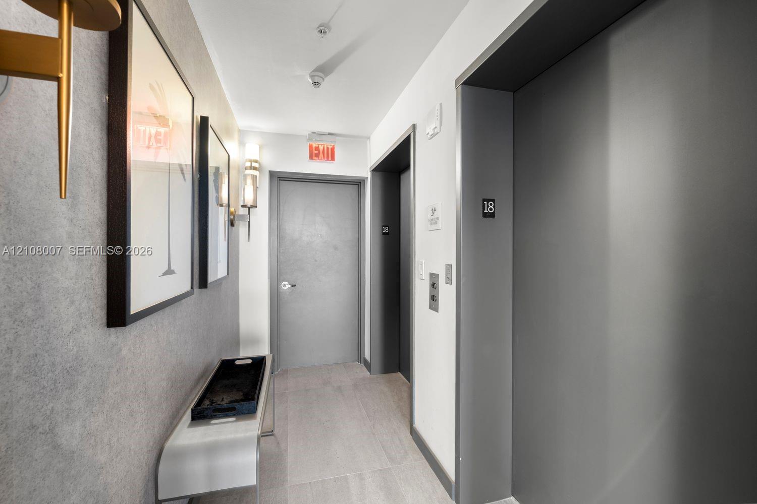 Hallway featuring neutral textured wall coverings, grey door finishes, tiled flooring, and dual wall-mounted light fixtures