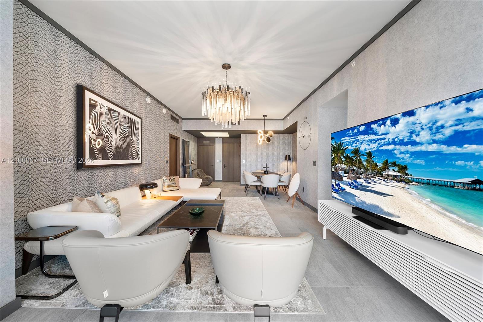 Textured wall coverings, crystal-accented chandelier, wood-finish flooring, custom-slatted built-in media console, and recessed ceiling lighting