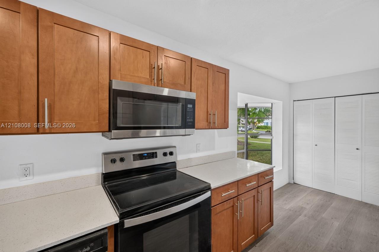 Kitchen featuring wood cabinetry, stone-finish countertops, stainless steel appliances, a recessed window, and wood-finish flooring