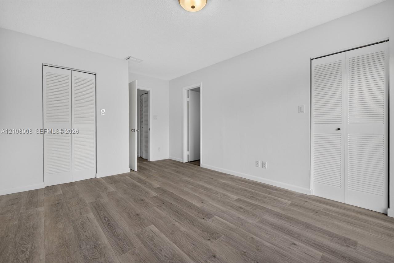 Wood-finish flooring, two sets of white louvered-door closets, and a flush-mount ceiling light fixture