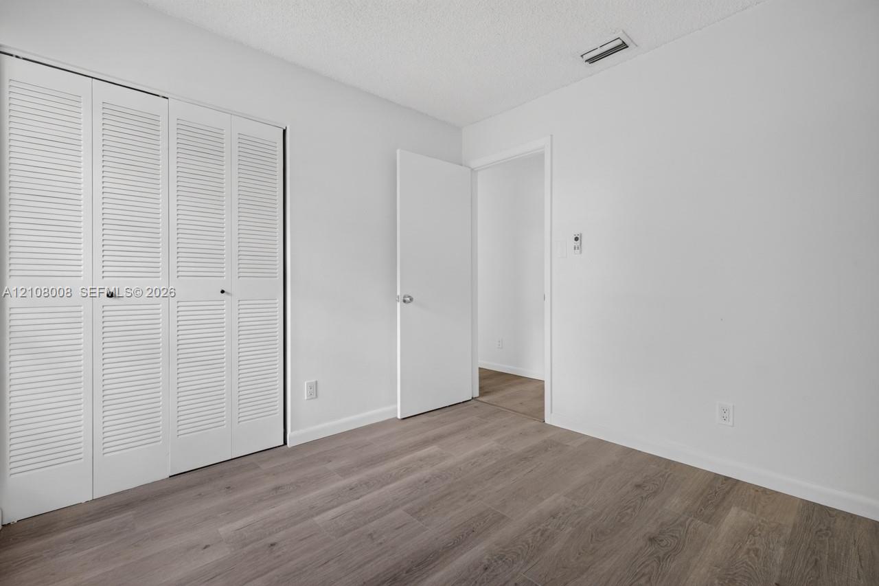 Interior space featuring wood-finish flooring, white walls, and a white louvered closet door