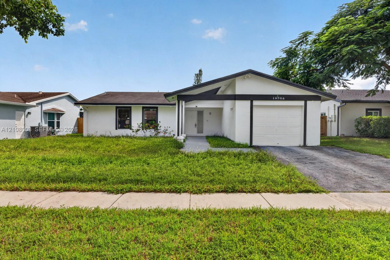 Single-story exterior featuring a painted masonry facade, a gabled roofline with dark trim, an attached garage, and a concrete driveway