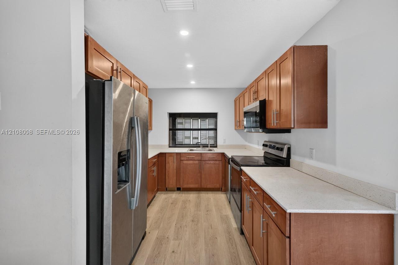 Kitchen featuring wood cabinetry, stone-finish countertops, stainless steel appliances, and light wood-finish flooring
