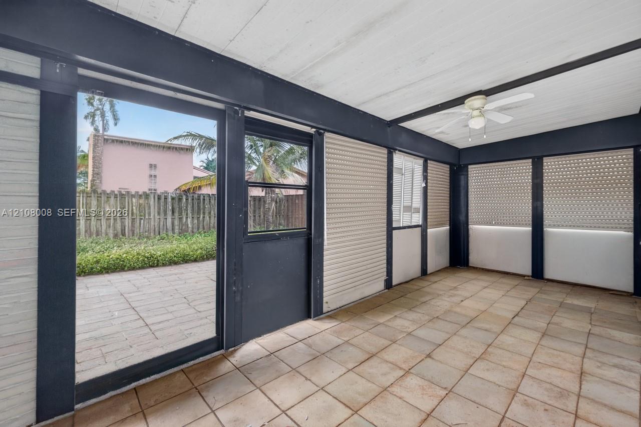 Enclosed patio featuring tile flooring, painted wood-panel ceiling, dark structural framing, ceiling fan, and sliding glass door access to a paved exterior area