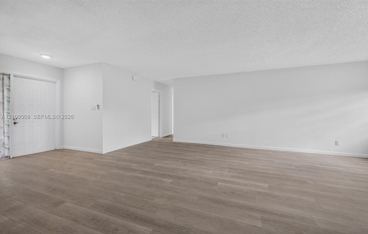 Open-concept interior featuring light wood-finish flooring, neutral wall tones, and an entry door with a six-panel design