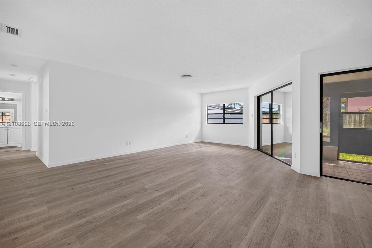 Open-concept area featuring wood-finish flooring, white walls, black-framed windows, and sliding glass doors with access to an exterior screened enclosure