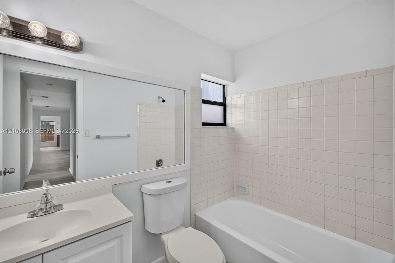 Full-width vanity with integrated sink, expansive wall-mounted mirror, three-light polished chrome fixture, and tiled tub surround