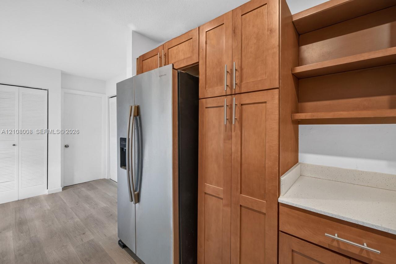 Stained wood cabinetry, stainless steel refrigerator, solid surface countertops, open shelving, and wood-finish flooring