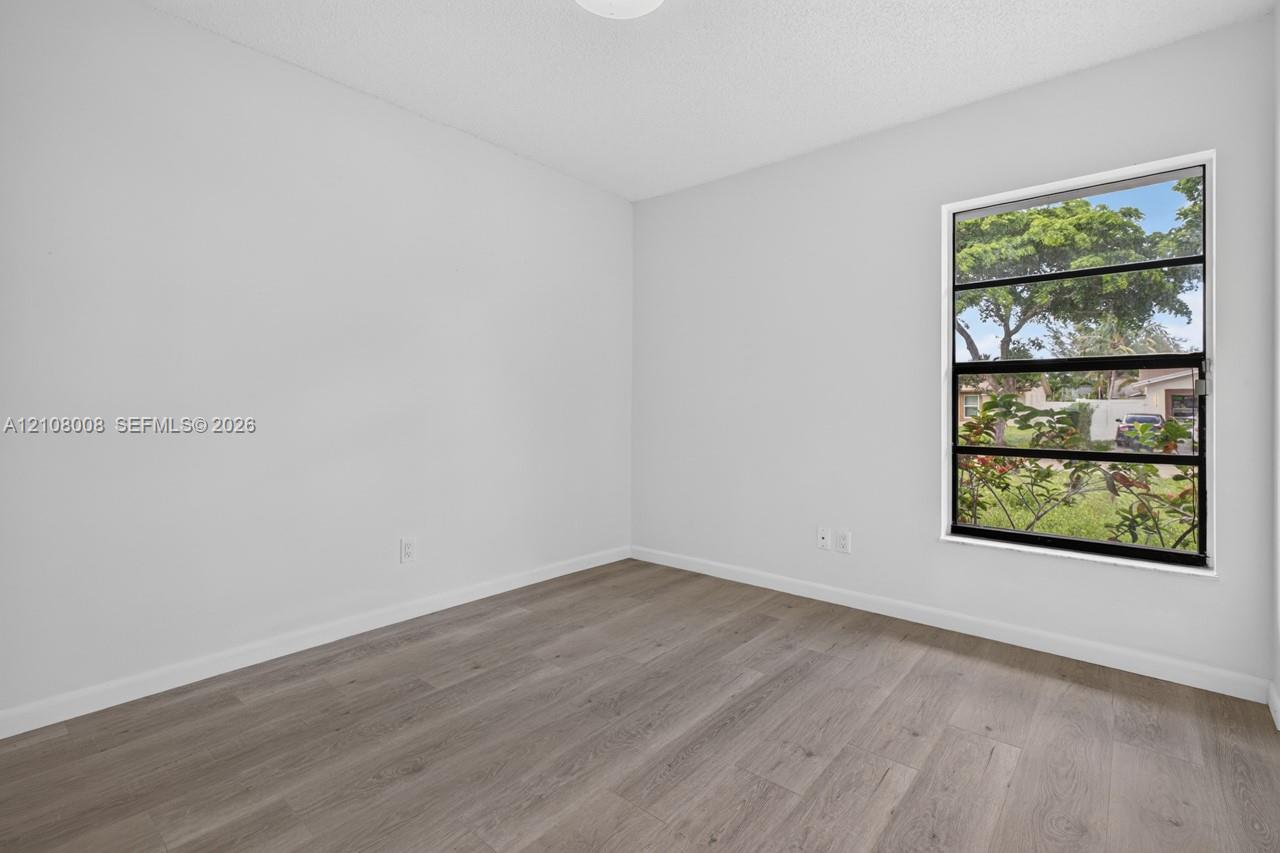 Neutral-toned interior space featuring wood-finish flooring, white walls, and a multi-pane horizontal window