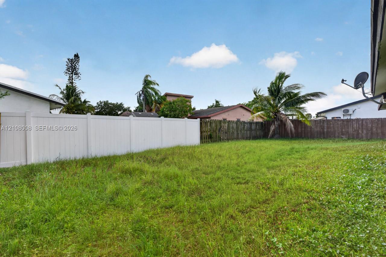 Open backyard area featuring a white vinyl privacy fence and mature palm trees
