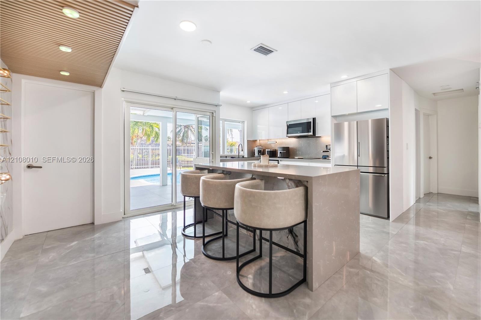 Kitchen featuring high-gloss cabinetry, stone-finish countertops, waterfall-edge island, stainless steel appliances, and large-format tile flooring