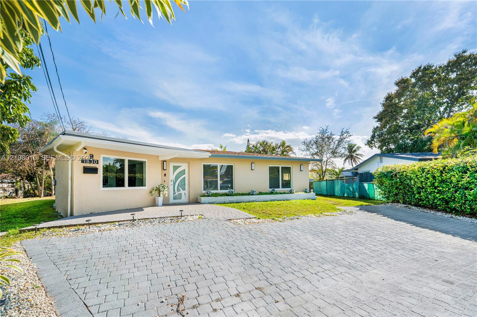 Single-story exterior featuring a light-toned stucco facade, paver driveway, decorative glass-paneled entry door, and manicured landscaping