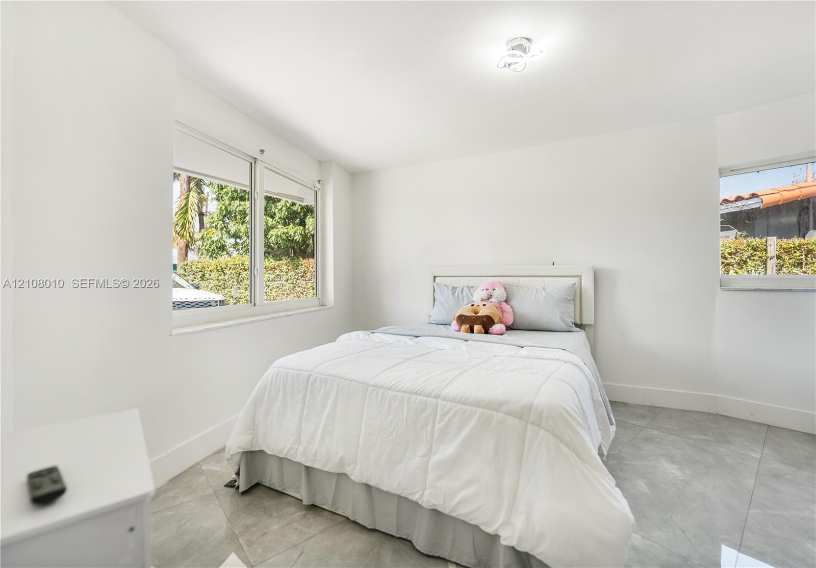 Neutral-toned interior space featuring large-format ceramic tile flooring, bright white wall finishes, sliding windows, and a flush-mount ceiling light fixture
