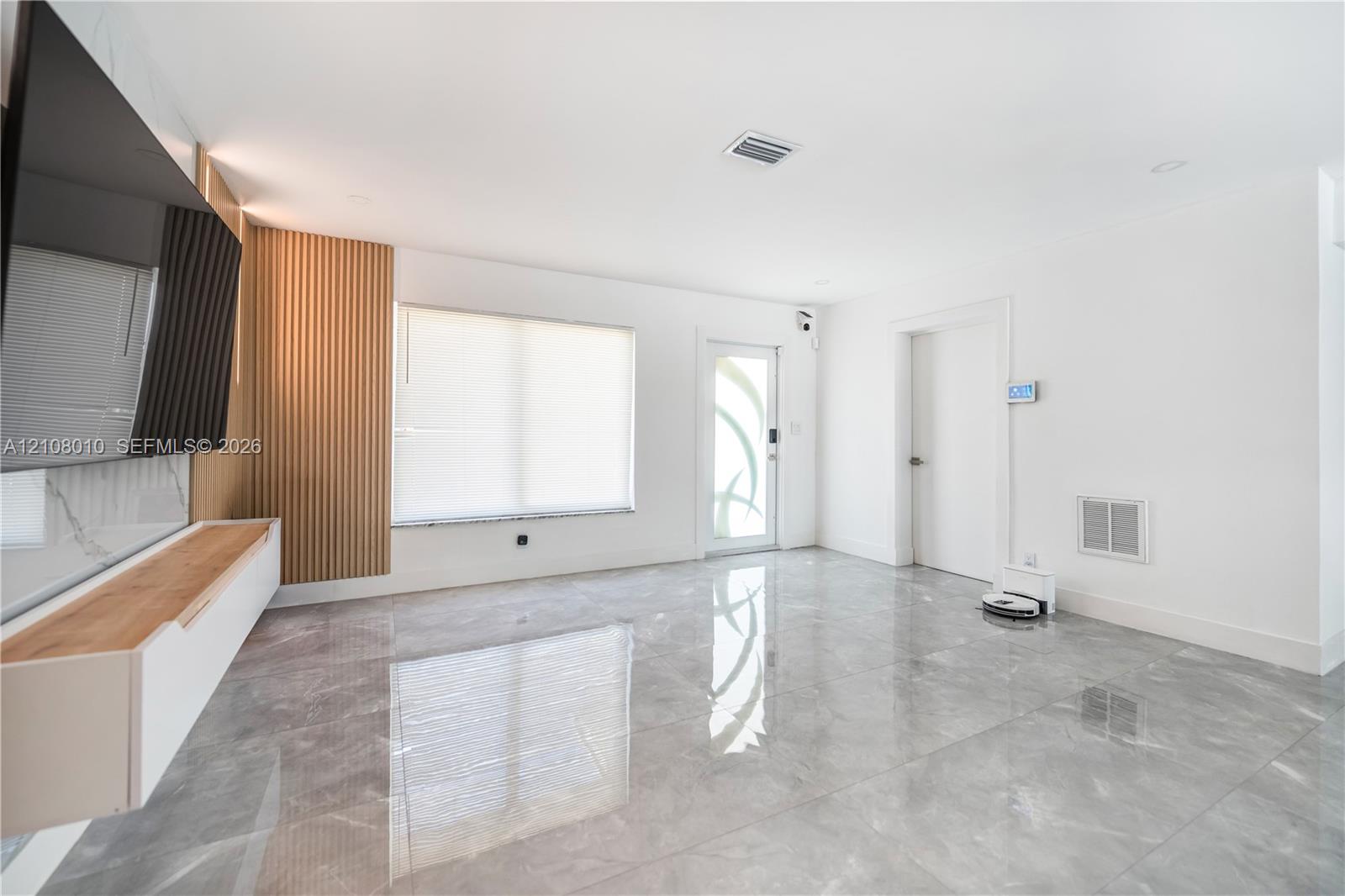 Large-format stone-style tile flooring, decorative vertical wood-slat accent wall, floating built-in media console, and glass-paneled entry door