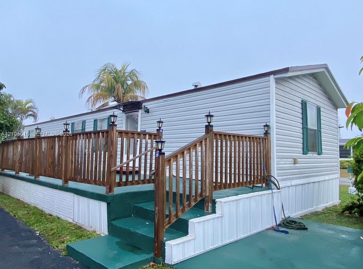 Exterior featuring horizontal light-toned siding, a full-length elevated wooden deck with integrated lighting, and a painted concrete staircase