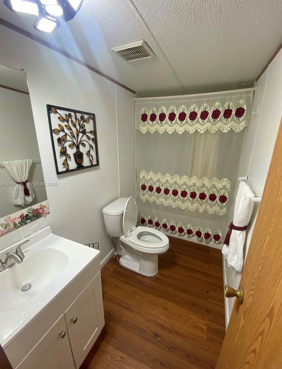 Bathroom featuring a white vanity cabinet with an integrated basin, wood-finish flooring, a combination tub and shower, and a mounted overhead light fixture