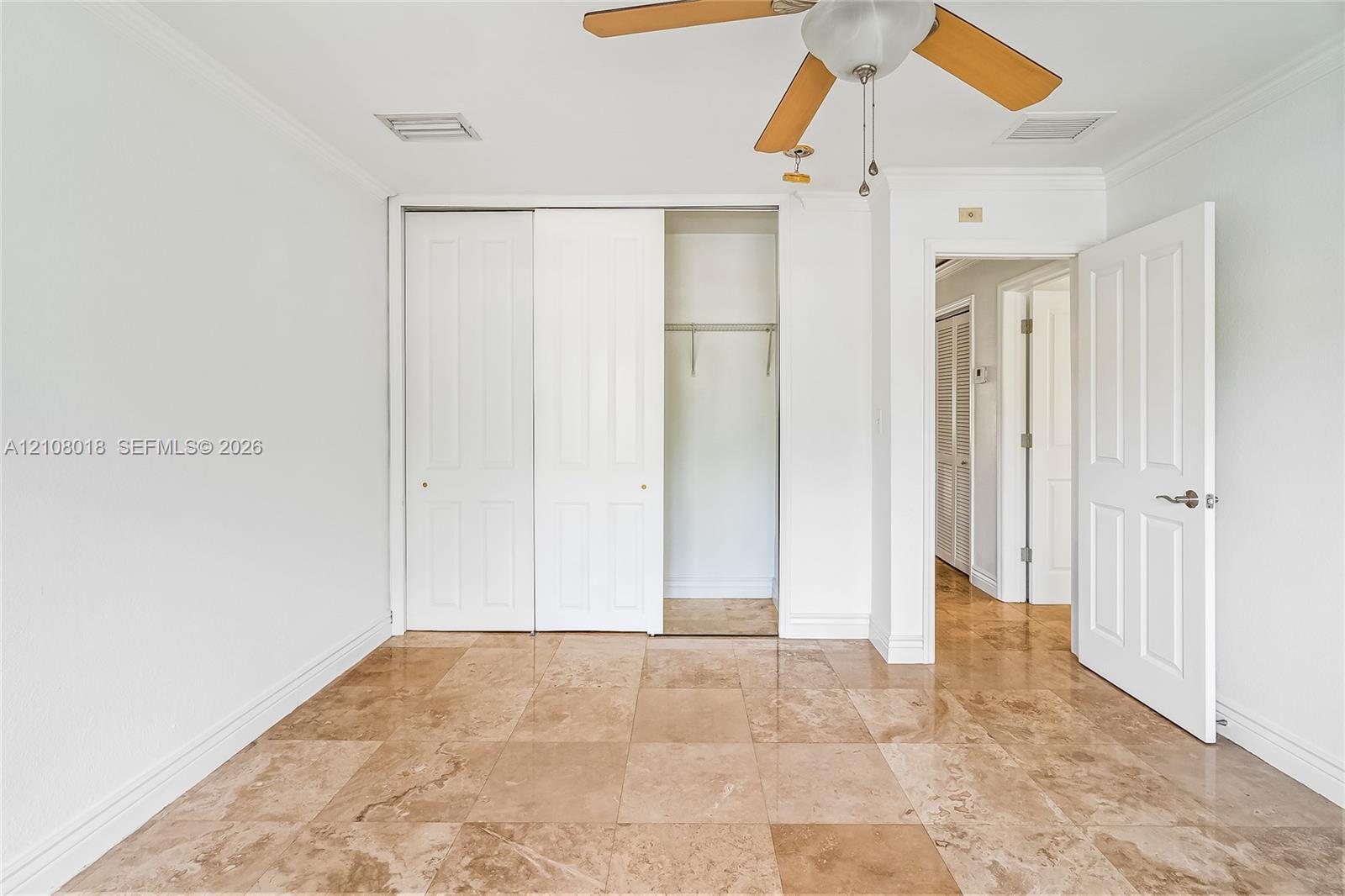Room featuring natural stone tile flooring, a dual-panel sliding closet, crown molding, and a ceiling fan with integrated lighting
