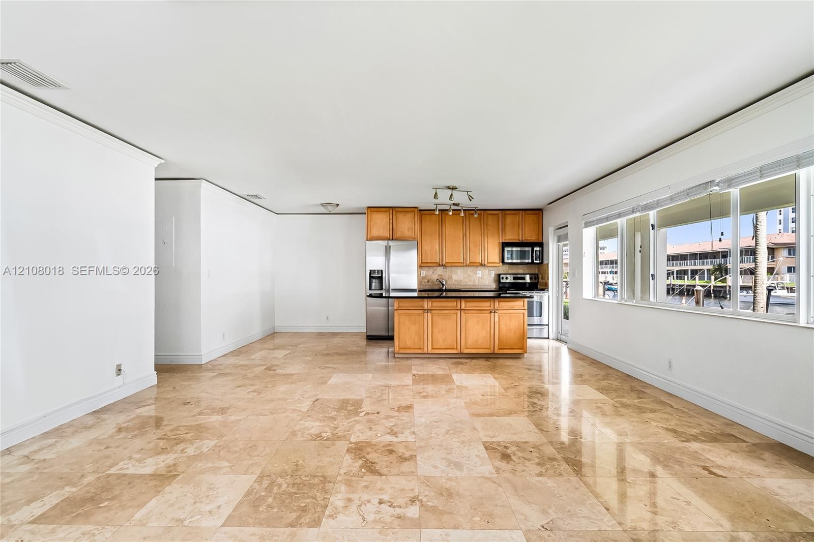Kitchen featuring light-finish cabinetry, dark solid-surface countertops, and stainless steel appliances, accented by large-format stone tile flooring and panoramic windows