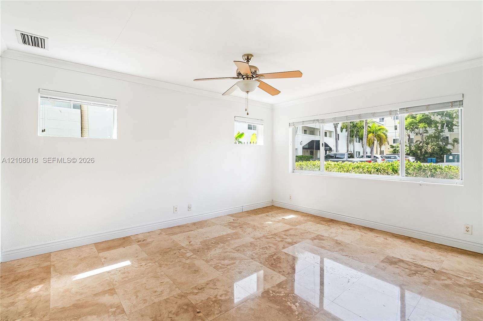Interior space featuring large-format polished tile flooring, neutral walls with crown molding, three windows with integrated blinds, and a central ceiling fan with an integrated light fixture