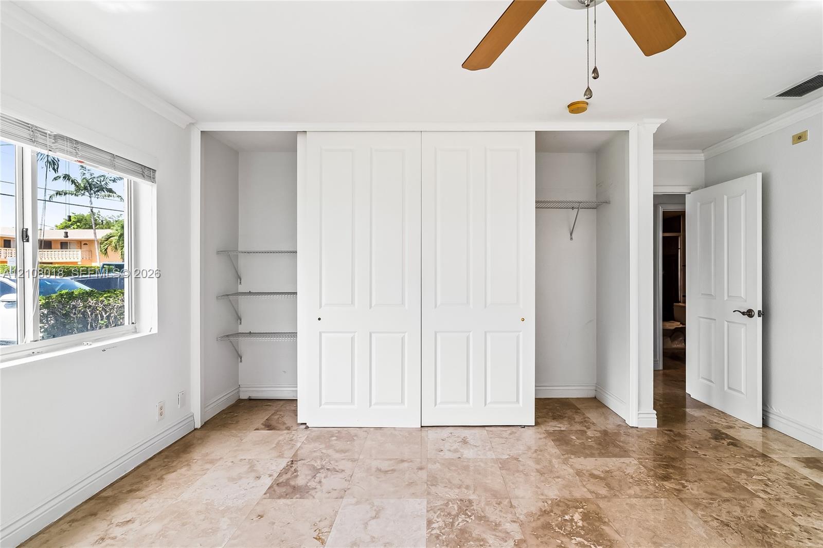 Room featuring neutral wall finishes, tile flooring, built-in dual-panel closet doors, wall-mounted shelving, and an overhead ceiling fan