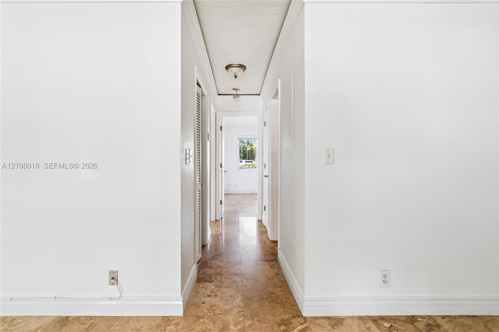 Hallway featuring natural stone flooring, crisp white walls, crown molding, and a flush-mount light fixture